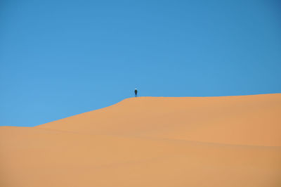 Distant view of person standing on sand dune against clear blue sky