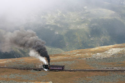 High angle view of train emitting smoke while moving against mountain