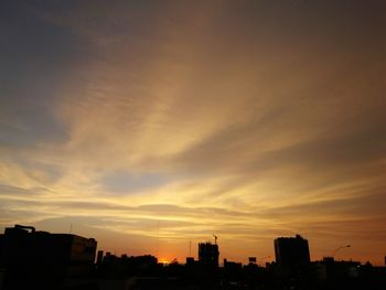 Silhouette of city against cloudy sky during sunset