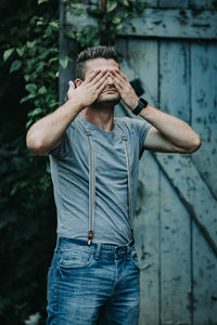 Young man with hands covering eyes standing against door