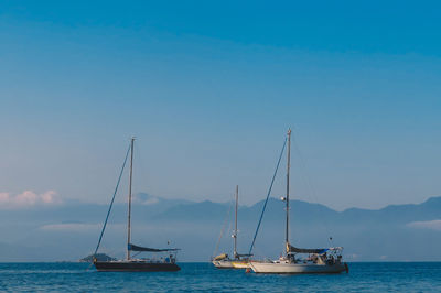 Boats sailing on sea against blue sky