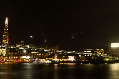 Illuminated bridge over river by buildings against sky at night