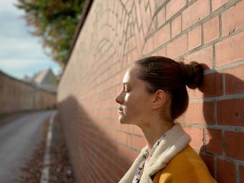 Young woman standing by brick wall