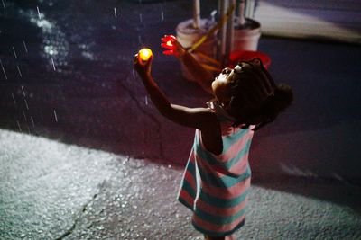 Side view of girl playing in rainfall at night