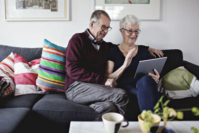 Smiling senior couple sitting on sofa sharing digital tablet in living room at home