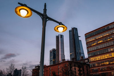 Low angle view of illuminated street light by building against sky