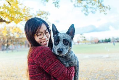 Smiling woman carrying dog while standing at park