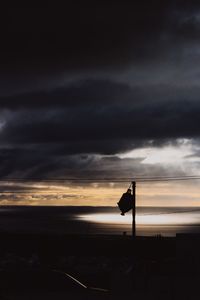 Silhouette flag on sea against sky at sunset