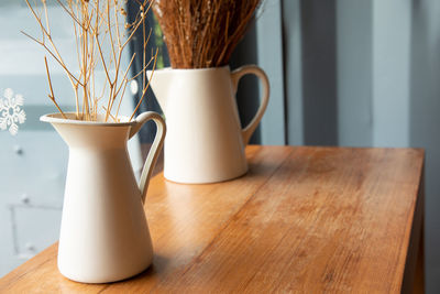 Cafe decorating with dried flowers in white ceramic jar on the wooden table near the glass window 