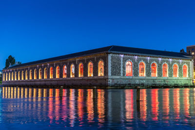 Reflection of illuminated building against clear blue sky