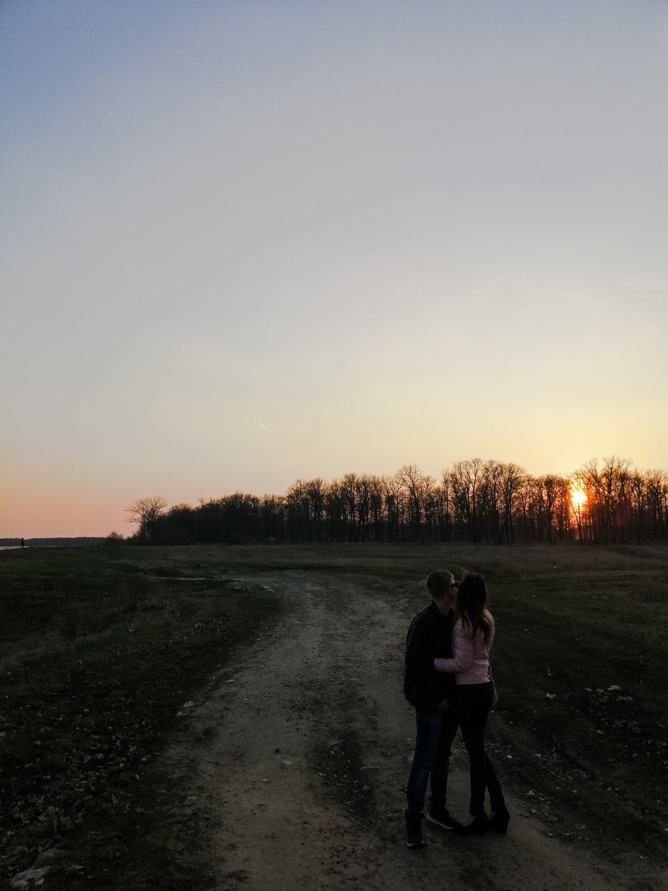 COUPLE STANDING ON SHORE AGAINST SKY AT SUNSET