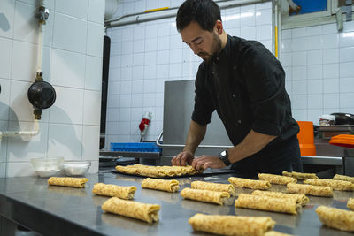 Chef arranging food rolls together in tray while standing at kitchen