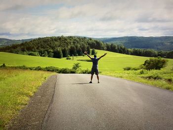 Rear view of man jumping on road against sky