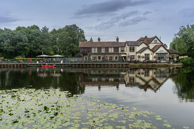 Reflection of house and trees by lake against sky