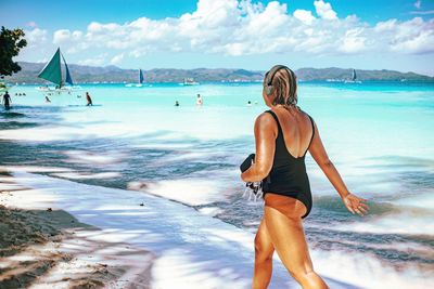 Rear view of woman standing on beach against sky