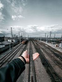 Cropped hand of person holding railroad tracks against sky