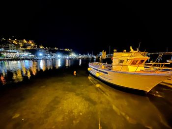 Boats moored on illuminated city by sea against sky at night