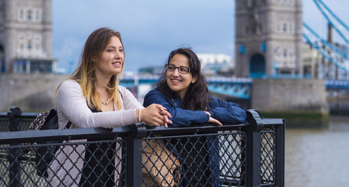 Smiling female friends talking while standing by railing in city