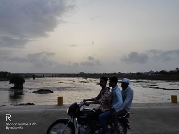 People riding motorcycle on water against sky