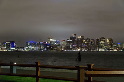 Illuminated cityscape by sea against sky at night