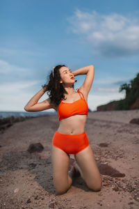 Portrait of young woman standing at beach against sky