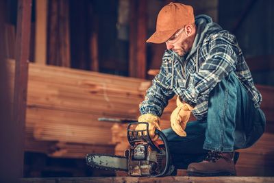 Low angle view of man crouching with chainsaw 