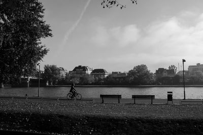 Woman riding bicycle by lake at park against sky