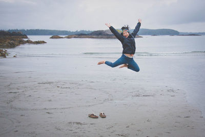 Portrait of young woman jumping on beach against sky