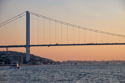 Suspension bridge over river against sky during sunset