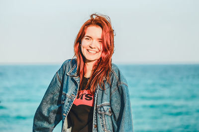 Portrait of smiling young woman standing against sea