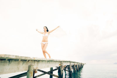 Full length of young woman standing on pier against sea