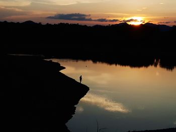 Silhouette trees by lake against sky during sunset