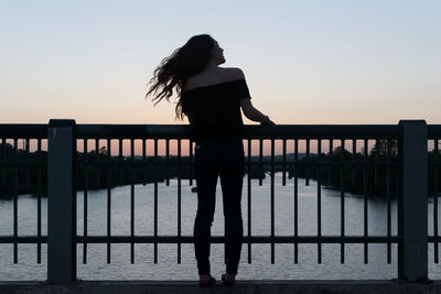 Silhouette woman standing on pier against sea during sunset