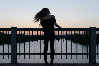 Rear view of woman standing in front of river at sunset