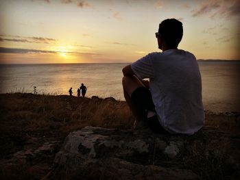 Rear view of couple sitting on beach against sky during sunset