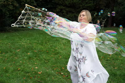 Smiling woman making bubbles while standing against trees