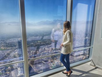 Rear view of woman standing by window in city