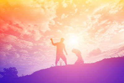 Silhouette couple standing against orange sky