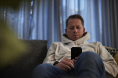 Ill man sitting on sofa with smartphone