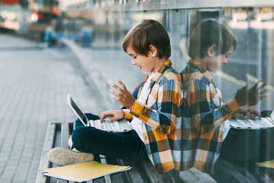 A happy boy is sitting on a bench, holding a laptop on his lap. the boy communicates