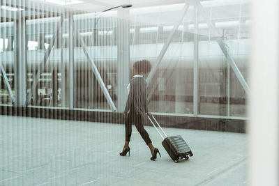 Woman seen through glass walking with luggage on railroad station