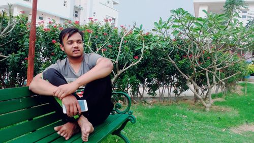 Man holding mobile phone while sitting on bench at park