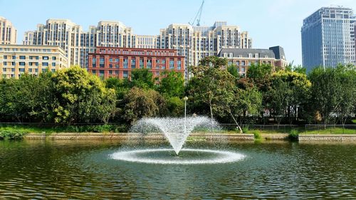 Fountain in park by buildings in city against sky