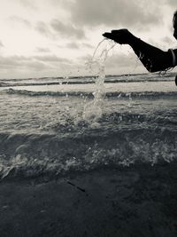 Silhouette man splashing water in sea against sky