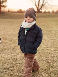 Small boy in snowsuit walking through field at sunset