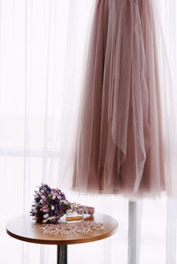 View of bridal gown with bouquet and perfume against curtain