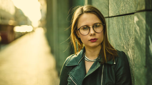 Portrait of beautiful young woman standing by wall