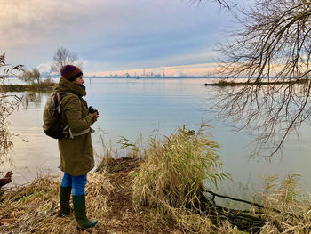 Side view of woman standing by lake against sky