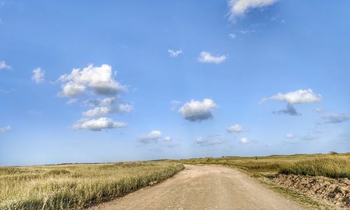 Empty road amidst field against sky