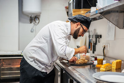 Side view of busy male cook using grater and garnishing sweet dessert placed on slate board in kitchen